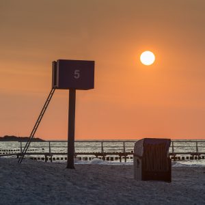 Strandkorb und Ausguck am menschenleeren Sandstrand von Heiligenhafen vor der untergehenden Sonne