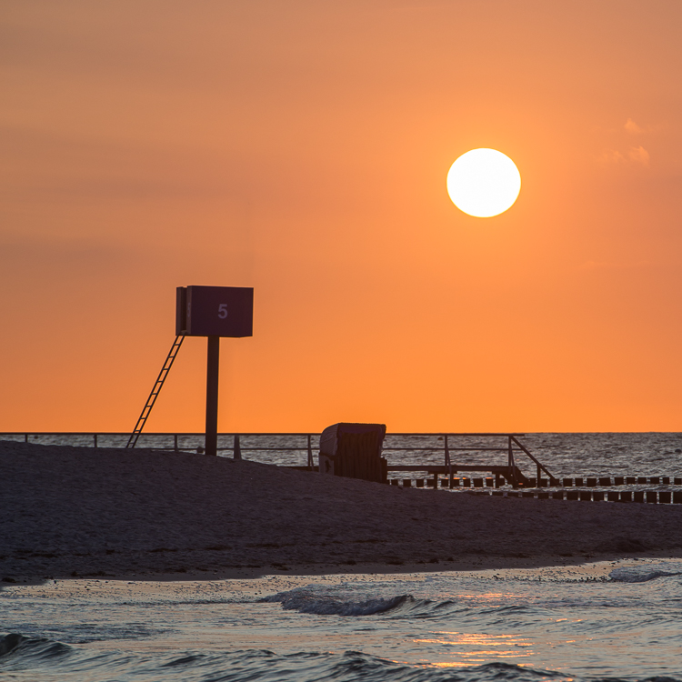 Strandkorb und Ausguck am menschenleeren Sandstrand vor der untergehenden Sonne, Heiligenhafen, Schleswig-Holstein, Deutschland