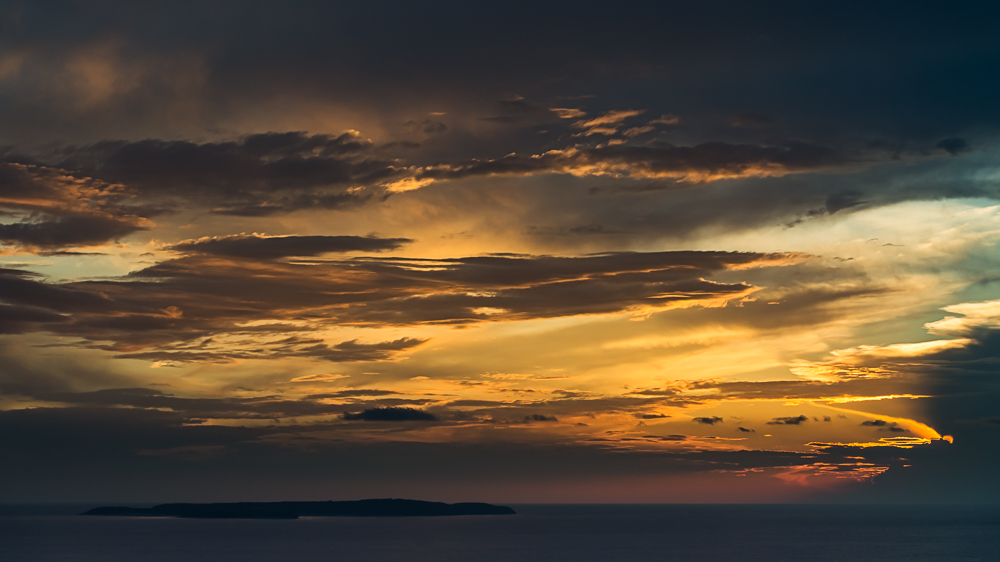 Die untergehende Sonne beleuchtet dramatisch die Wolken über der Insel Susak im adriatischen Meer der Kvarner Bucht, Kroatien