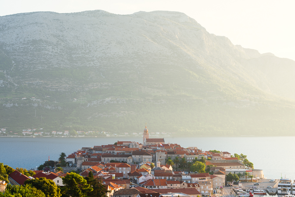 Die Altstadt von Korčula vor dem Gebirgsmasssiv des Sv. Ilija auf der Halbinsel Pelješac im Gegenlicht der Morgensonne, Insel Korčula, Süddalmatien, Kroatien