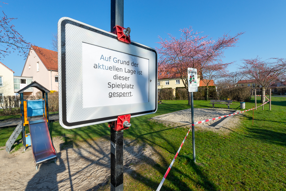 Verbotsschild und rot-weisses Absperrband an einem gesperrten Kinderspielplatz während der Corona-Krise in Deutschland