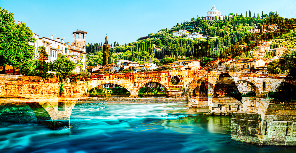 Die römische Ponte Pietra über dem Fluß Etsch in der Altstadt von Verona vor mediterraner Landschaft in der Morgensonne, Venetien, Italien