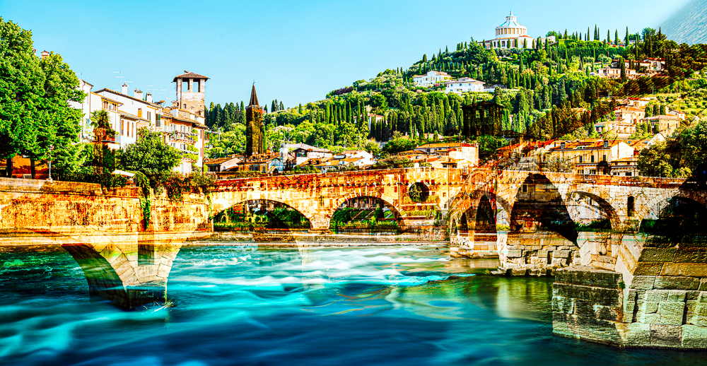 Die römische Ponte Pietra über dem Fluß Etsch in der Altstadt von Verona vor mediterraner Landschaft in der Morgensonne, Venetien, Italien