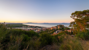 Blick über die Bastion, die Stadt und den Hafen von Castiglione della Pescaia auf eine weit geschwungene Bucht der Küste der Maremma bei Sonnenaufgang, Toskana, Italien