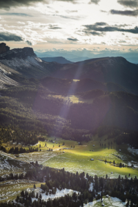 Sonne strahlt durch Wolken auf eine Herbstlandschaft der Dolomiten mit Gampenalm, Geisleralm, Raschötz und Seceda der Puez-Geisler-Gruppe, Villnößtal, Südtirol, Italien
