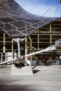 Mann sitzt auf einer Betonbefestigungen der Stahlseile des Zeltdachs der Olympiahalle im Olympiapark, München, Deutschland