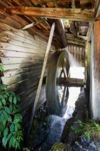 Wasser treibt ein hölzernes Wasserrad einer historischen Getreidemühle im Mühlental von Campill an, Südtirol, Italien