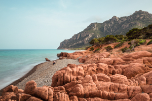 Der graue Kieselstrand Coccorocci umrahmt von roten Porphyrfelsen und den Wäldern um den Monte Cartucceddu an der Ostküste von Sardinien, Ogliastra, Italien