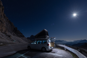 Van mit Dachzelt unterhalb der Drei Zinnen mit Aussicht nach Süden auf Bergketten und Gipfel der Dolomiten im hellen Mondlicht, Italien