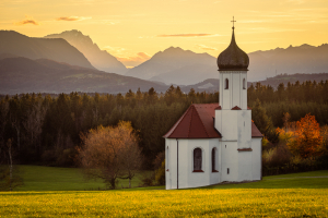 Die Kapelle St. Johann oberhalb des Loisachtals, dem Kochelsee und den herbstlichen bayrischen Alpen mit der Zugspitze in der Abendsonne, Deutschland