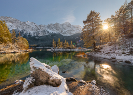 Verschneite Bergwälder und das Wetterstein-Bergmassiv in der Nachmittagssonne spiegeln sich im türkisfarbenen Wasser des Eibsees, Bayern, Deutschland