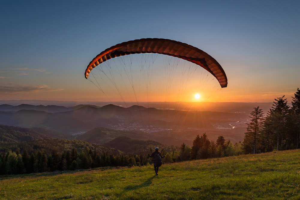 Gleitschirmflieger am Startplatz der Teufelsmühle im Murgtal im Schwarzwald beim Start in den Sonnenuntergang, Baden-Württemberg, Deutschland