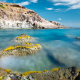 Mediterrane Naturschönheit - Zerklüftete, bunte Felsformationen in der Brandung des tiefblauen Mittelmeers an der Westküste von Sardinien, Italien