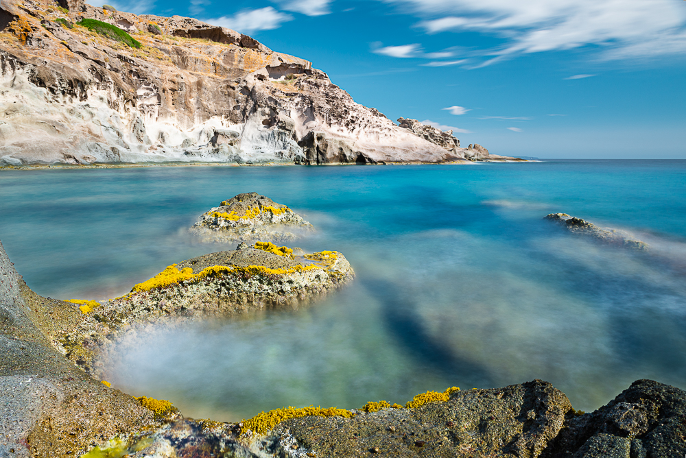 Mediterrane Naturschönheit - Zerklüftete, bunte Felsformationen in der Brandung des tiefblauen Mittelmeers an der Westküste von Sardinien, Italien