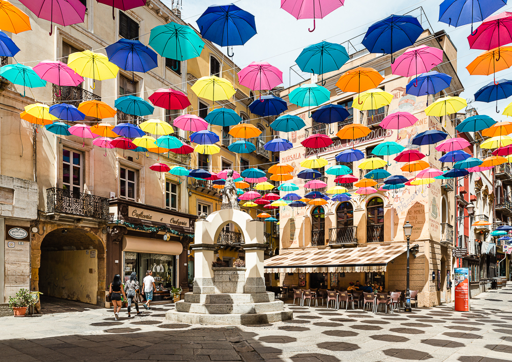 Bunte Sonnenschirme schützen die Passanten auf der von historischen Häusern umgebenen Piazza Lamarmora der Altstadt von Iglesias im Südwesten von Sardinien vor der heißen Mittagssonne, Iglesiente, Italien