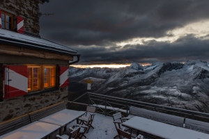 Das erste Sonnenlicht der Morgendämmerung in den Wolken über dem Ramolhaus mit Blick auf den wolkenverhangenen Alpenhauptkamm der Ötztaler und Stubaier Alpen, Gurgler Tal, Ötztaler Alpen, Tirol, Österreich