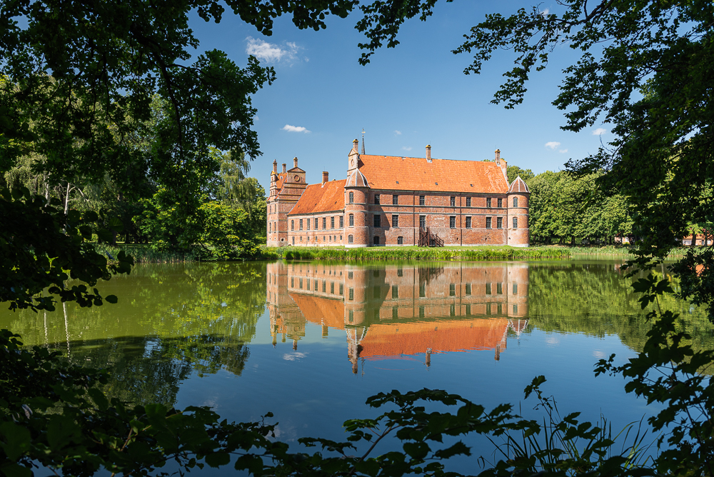 Die Renaissance Fassade von Schloss Rosenholm und spiegelt sich im Wasser, umrahmt von Blättern, Jütland, Dänemark