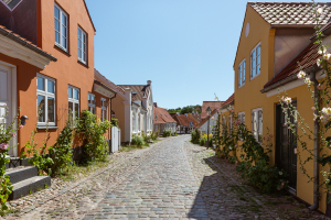 Bunte Fassaden und Stockrosen in den Gassen der Altstadt von Ebeltoft, Djursland, Dänemark in der Sonne vor blauem Himmel