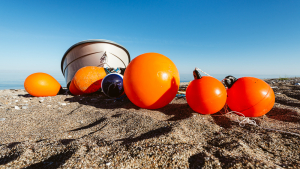 Orange Bojen und ein Fischerboot liegen auf einem Sandstrand am Ufer der Ostsee in der Sonne, Djursland, Jütland, Dänemark