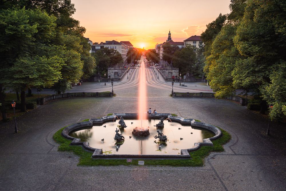 Springbrunnen mit Wasserfontänen vor der Luitpoldbrücke und Prinzregentenstrasse im Gegenlicht des Sonnenuntergangs in München