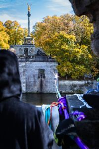 Ein Mann beobachtet einen anderen Mann auf einer Slackline über der Isar an der Luitpoldbrücke