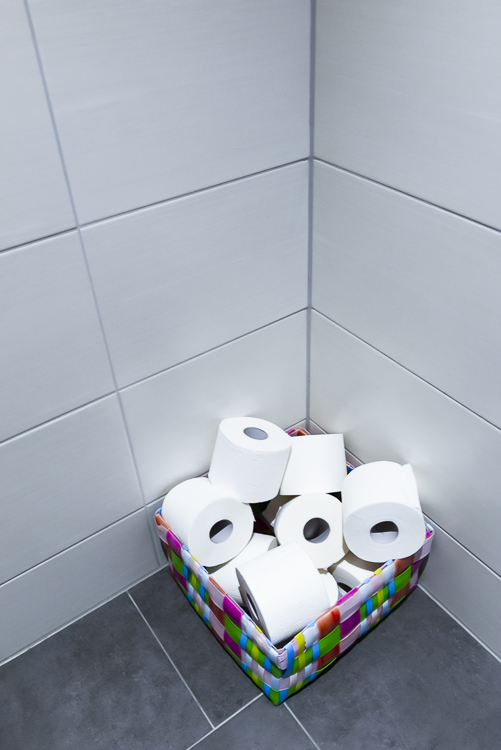 Ein Haufen Klopapierrollen in einem bunten Korb in der Ecke einer Toilette