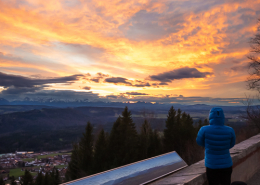 Eine Person neben der Panoramakarte schaut auf das Alpenpanorama vom Hohenpeißenberg bei Sonnenuntergang, Bayern, Deutschland