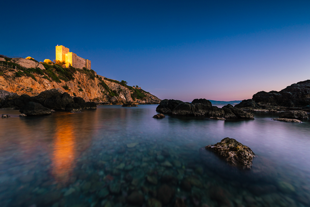 Die Burg Rocca Aldobrandesca an der Felsenküste der Maremma in Talamone im Zweilicht der Abenddämmerung, Toskana, Italien