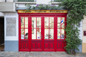 Eine leuchtend rote Eingansgtür zu einem Friseurgeschäft in der Altstadt von Céret im Roussillion, Okzitanien, Frankreich