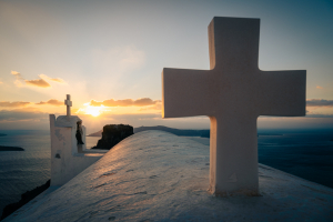 Kreuze und Glockenturm auf dem Dach der Kapelle des Heiligen Johannes des Enthaupteten im Gegenlicht des Sonnenuntergangs, Imerovigli, Santorin, Griechenland