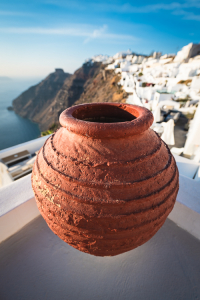 Ein großer runder Terrakotta Blumentopf vor den weissen Häusern von Imerovigli auf der Steilküste von Santorin, Kykladen, Griechenland