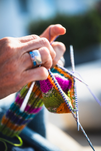 Hände einer Frau mit weisser Haut beim Stricken mit silbernen Stricknadeln und bunter Wolle