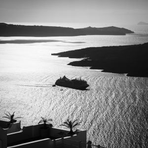 Ein Kreuzfahrtschiff liegt in der Caldera von Santorin im Gegenlicht der Sonne vor Anker, Kykladen, Griechenland