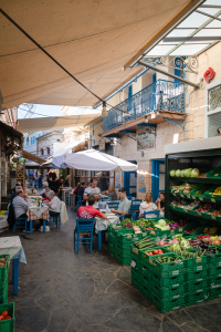 Gemüsehändler und Restaurants in einer blebten, engen Gasse im Hafenviertel von Ägina, Griechenland