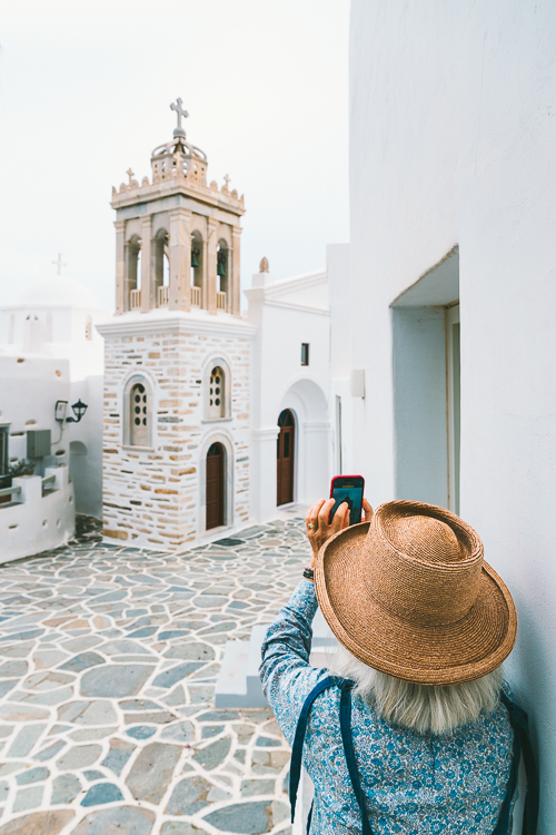 Eine Frau mit Hut fotografiert die Evangelismos Kirche in der Altstadt von Marpissa, Paros, Griechenland Eine Frau mit Hut fotografiert die Evangelismos Kirche in der Altstadt von Marpissa, Paros, Griechenland