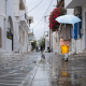 Eine Frau läuft mit einem Regensschirm durch eine Gasse in der Altstadt von Antiparos, Kykladen, Griechenland