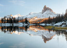 Golden leuchten die Lärchen vor der markanten Felsspitze des Becco di Mezzodi und spiegeln sich im Federa-See in den verschneiten Dolomiten bei Cortina d'Ampezzo, Italien