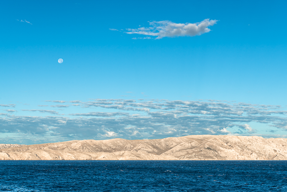 Blick auf den Mond über der Insel Krk an einem sonnigen Sommermorgen, Senj, Kroatien Blick auf den Mond über der Insel Krk an einem sonnigen Sommermorgen, Senj, Kroatien