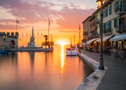 Golden geht Sonne genau hinter der Einfahrt zum Alten Hafen von Lazise am Gardasee unter; Venetien, Italien