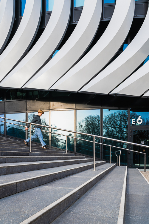 Ein Junge steigt eine Außentreppe vor der modernen Aluminium- und Glasfassade der SAP Garden Mehrzweckhalle herab, Olympiapark München, Deutschland Ein Junge steigt eine Außentreppe vor der modernen Aluminium- und Glasfassade der SAP Garden Mehrzweckhalle herab, Olympiapark München, Deutschland